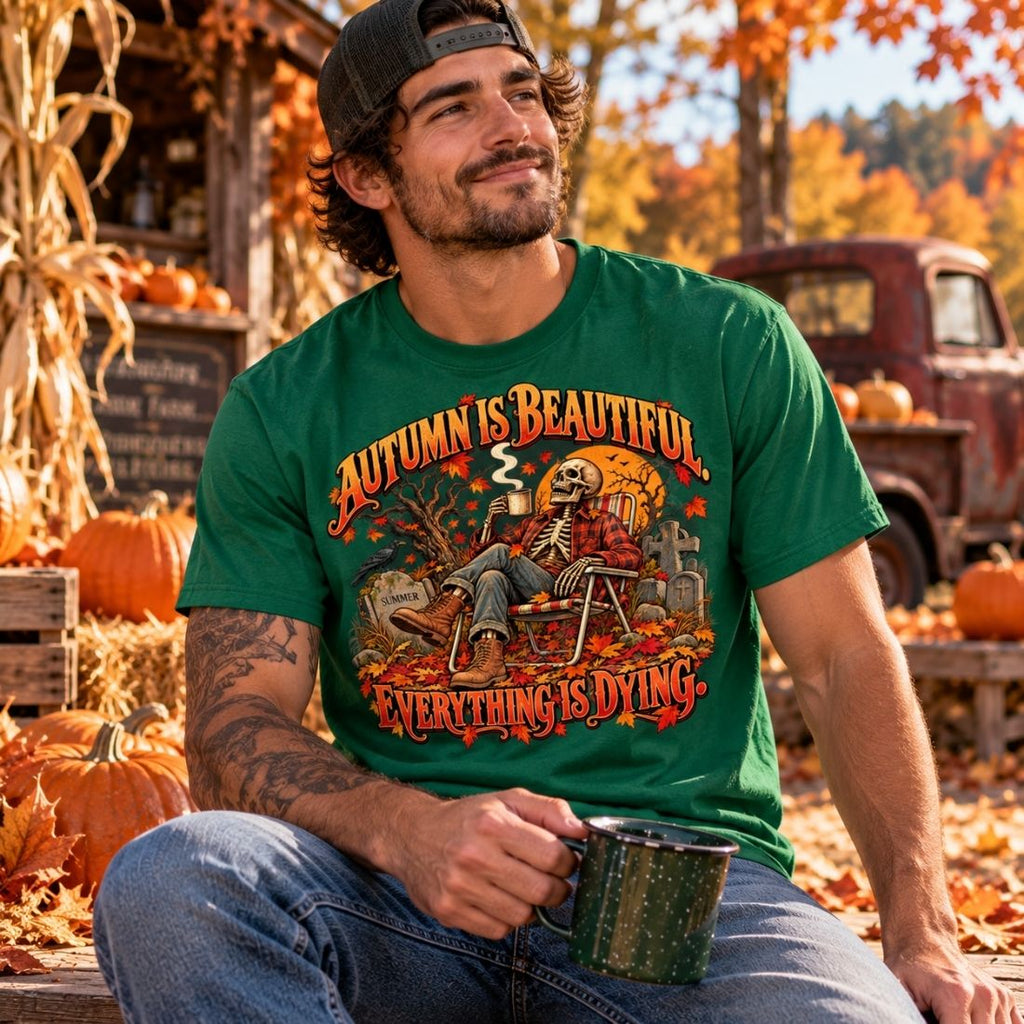 Model wearing a green Autumn Is Beautiful drop-shoulder T-shirt and jeans, seated with a mug beside pumpkins and fall leaves.