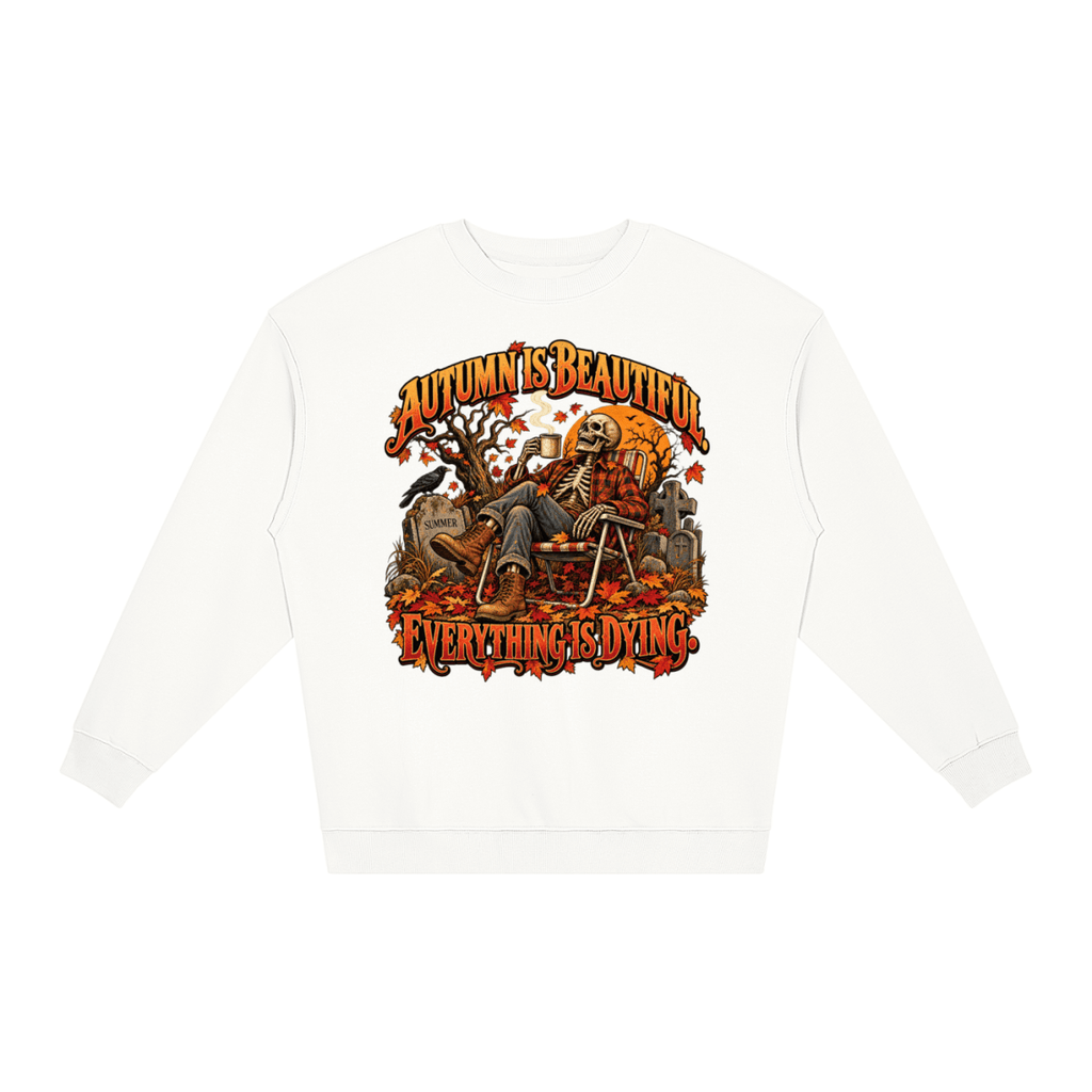 White Autumn Is Beautiful Everything Is Dying loose crewneck sweatshirt, front view with a seated skeleton surrounded by autumn leaves beneath Autumn Is Beautiful Everything Is Dying lettering.