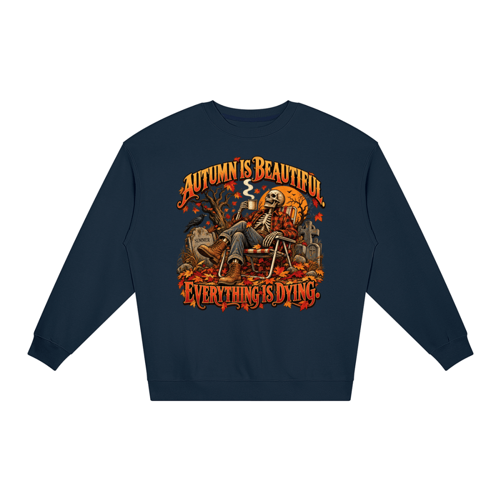 Navy blue Autumn Is Beautiful Everything Is Dying loose crewneck sweatshirt, front view with a seated skeleton surrounded by autumn leaves beneath Autumn Is Beautiful Everything Is Dying lettering.