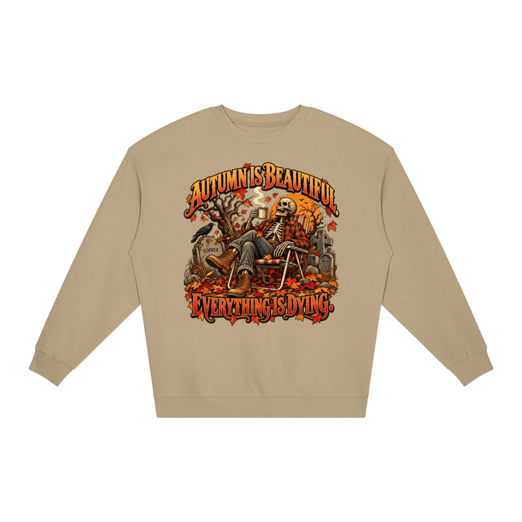 Khaki Autumn Is Beautiful Everything Is Dying loose crewneck sweatshirt, front view with a seated skeleton surrounded by autumn leaves beneath Autumn Is Beautiful Everything Is Dying lettering.