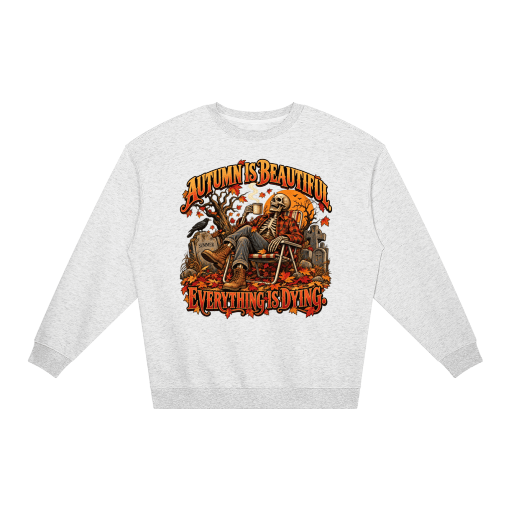 Light gray Autumn Is Beautiful Everything Is Dying loose crewneck sweatshirt, front view with a seated skeleton surrounded by autumn leaves beneath Autumn Is Beautiful Everything Is Dying lettering.