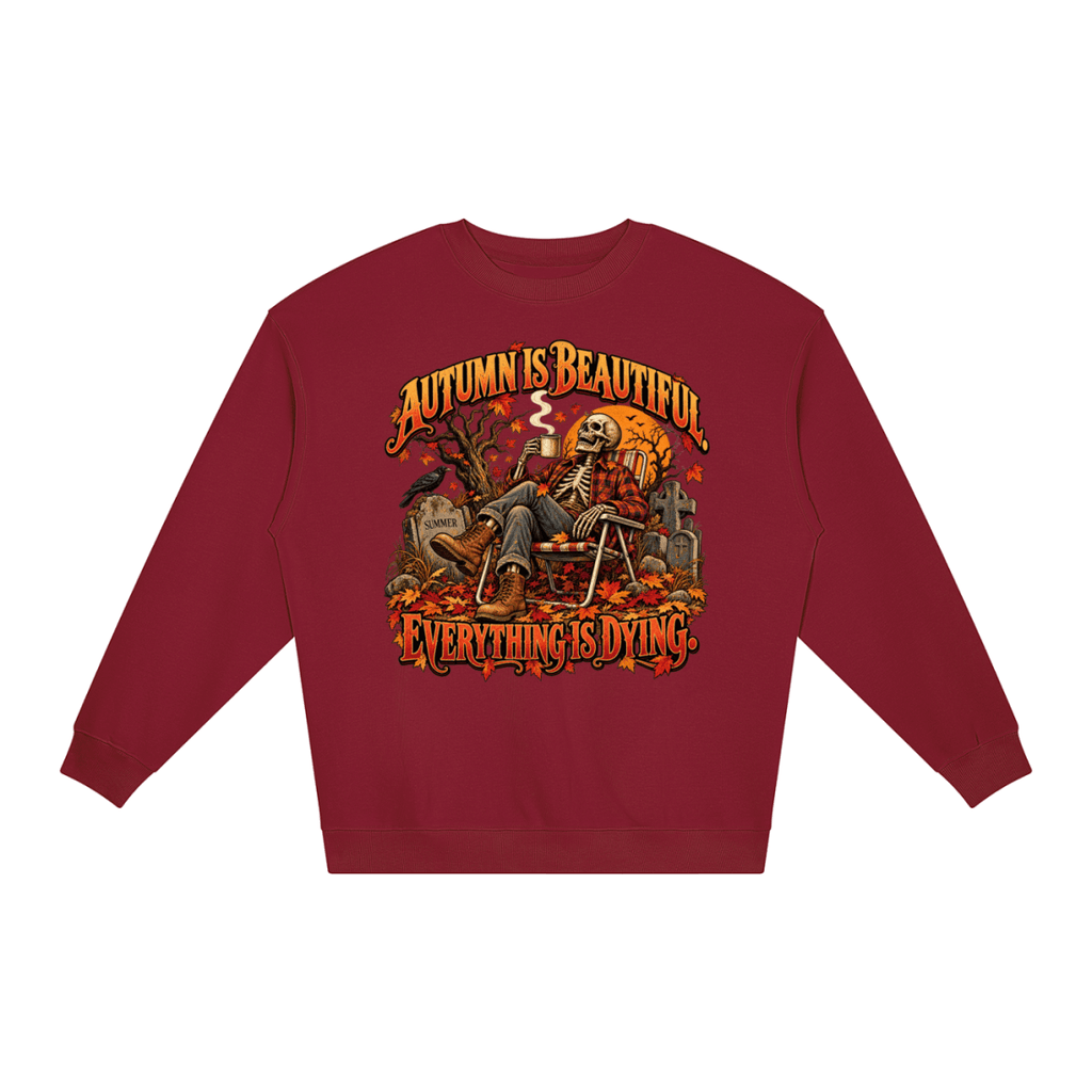 Burgundy Autumn Is Beautiful Everything Is Dying loose crewneck sweatshirt, front view with a seated skeleton surrounded by autumn leaves beneath Autumn Is Beautiful Everything Is Dying lettering.