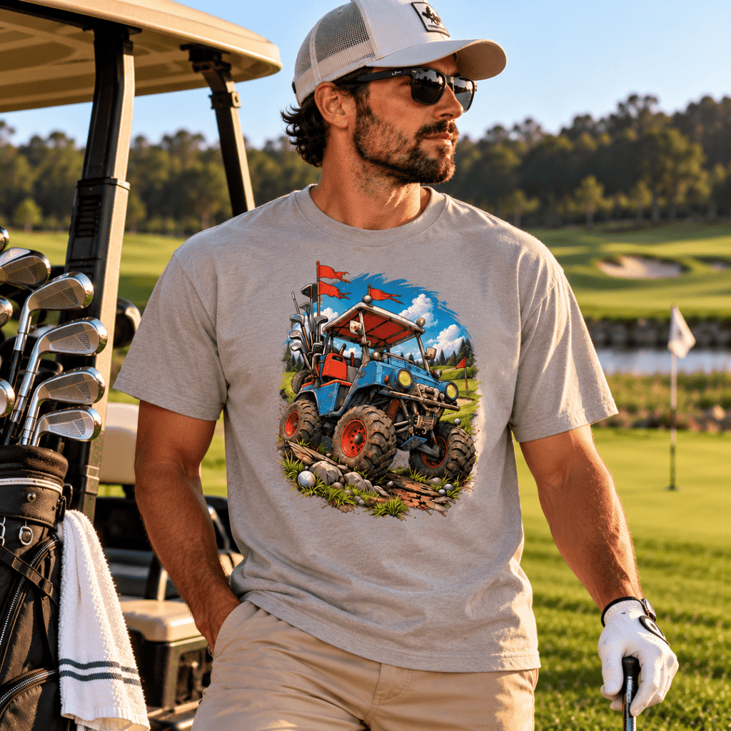 Model wearing a gray Battle-Hardened Golf Cart drop-shoulder T-shirt, beige pants and a golf glove beside a cart on a golf course.