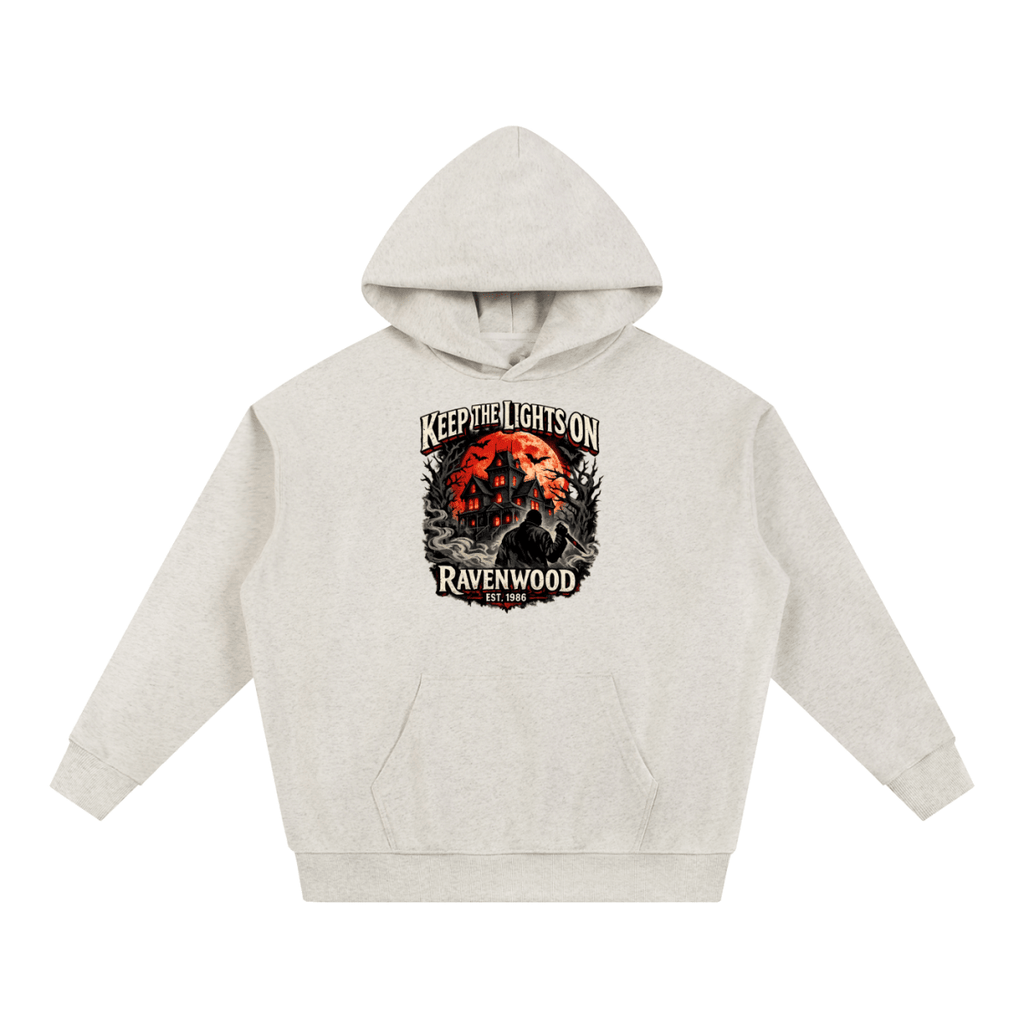 Oatmeal heavyweight hoodie, front view with a haunted house, orange moon and knife-holding silhouette with Keep the Lights On and Ravenwood Est. 1986 lettering.