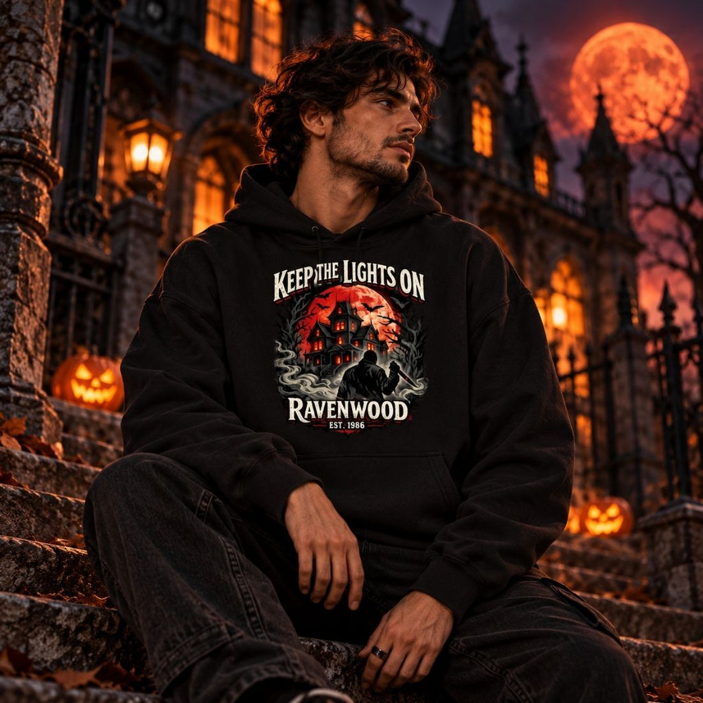 Seated model wearing a black Ravenwood Keep the Lights On hoodie outside a Gothic building with pumpkins and an orange moon.