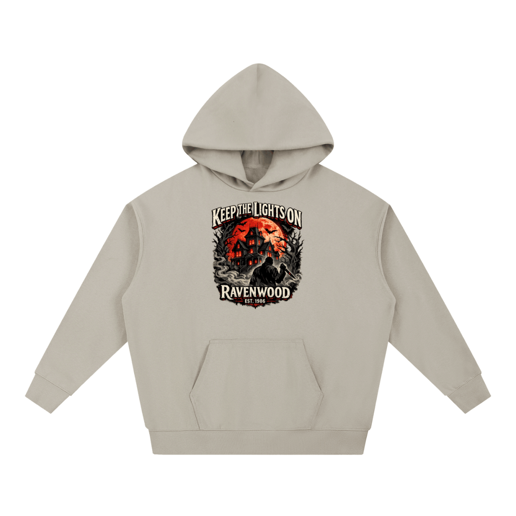 Gray beige heavyweight hoodie, front view with a haunted house, orange moon and knife-holding silhouette with Keep the Lights On and Ravenwood Est. 1986 lettering.