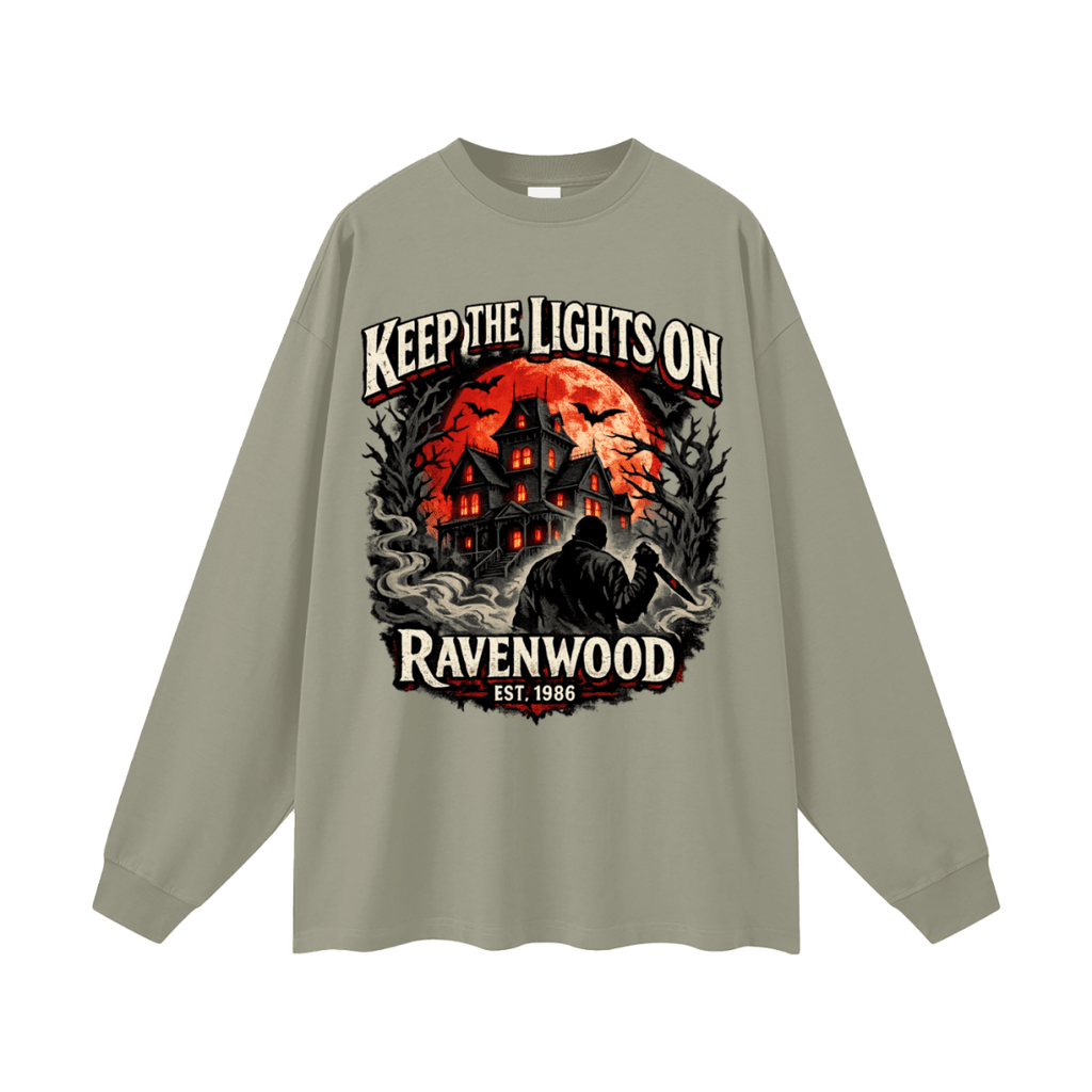 Sage green oversized long-sleeve T-shirt, front view with a haunted house, orange moon and knife-holding silhouette with Keep the Lights On and Ravenwood Est. 1986 lettering.