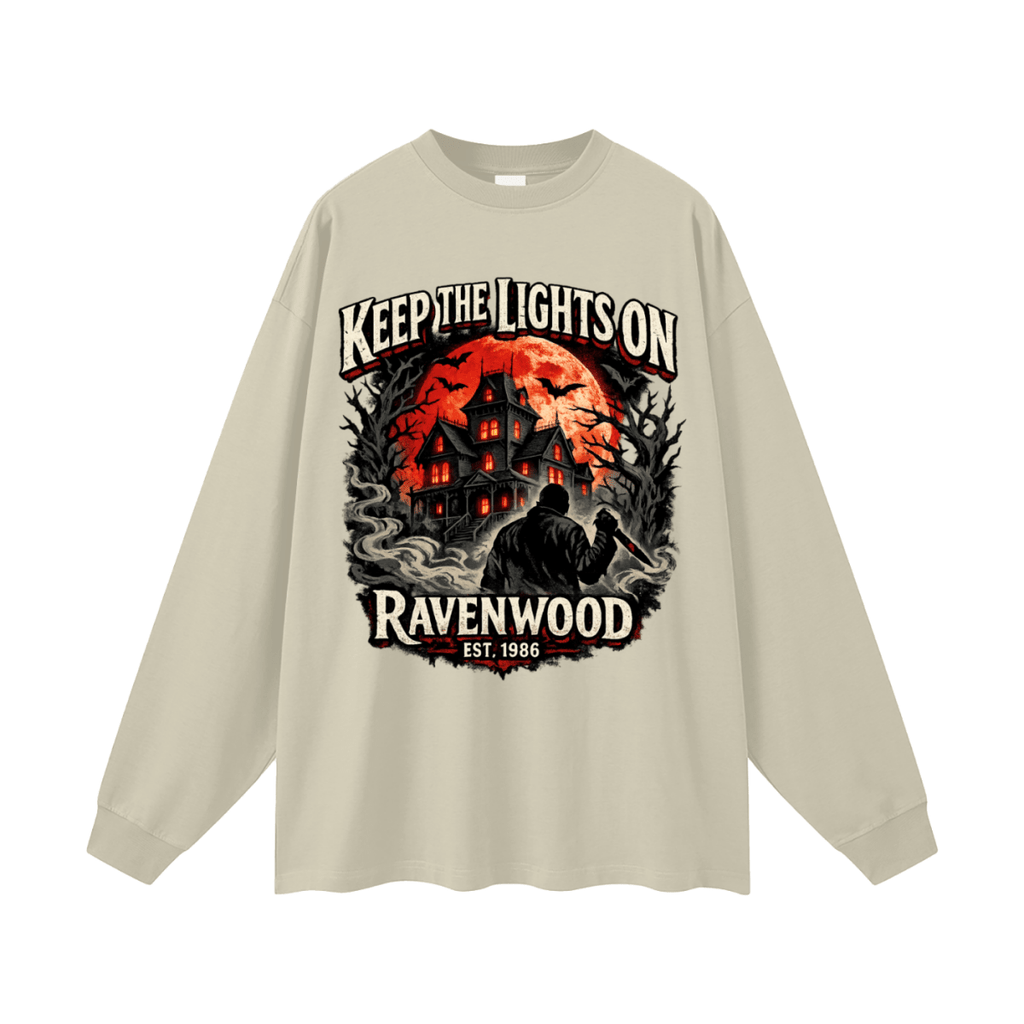 Beige oversized long-sleeve T-shirt, front view with a haunted house, orange moon and knife-holding silhouette with Keep the Lights On and Ravenwood Est. 1986 lettering.