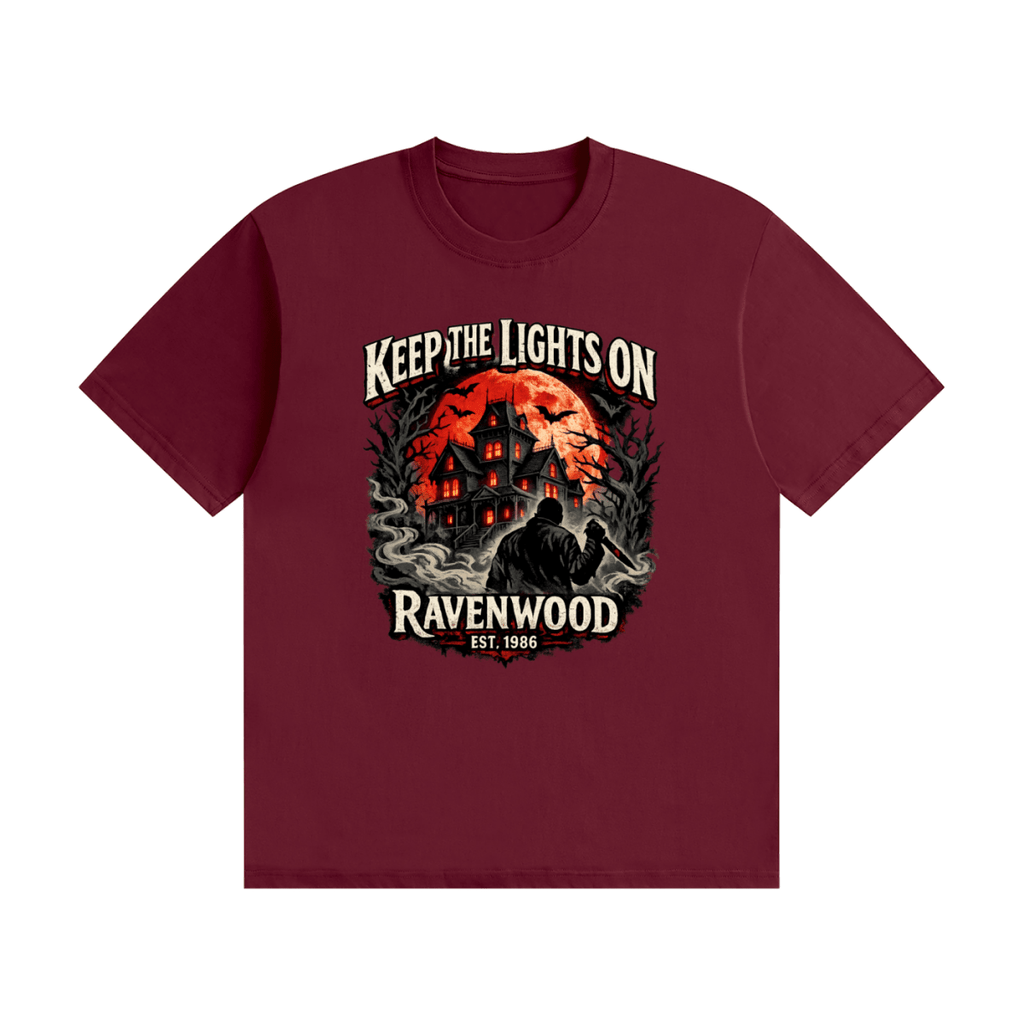 Burgundy cotton T-shirt, front view with a haunted house, orange moon and knife-holding silhouette with Keep the Lights On and Ravenwood Est. 1986 lettering.
