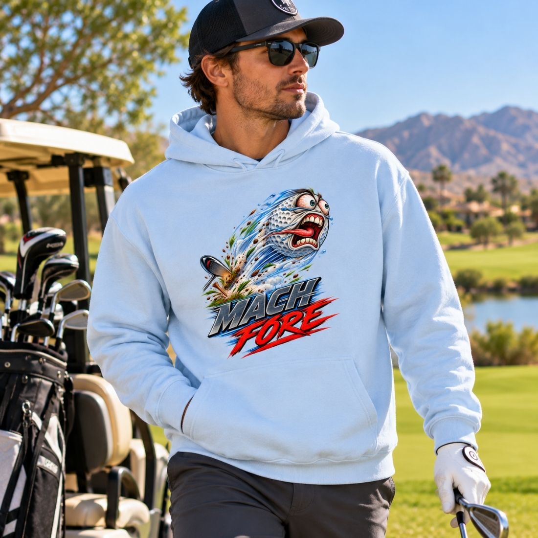 Model wearing a light blue Mach Fore Funny Golf hoodie, dark pants, cap and sunglasses beside a golf cart.