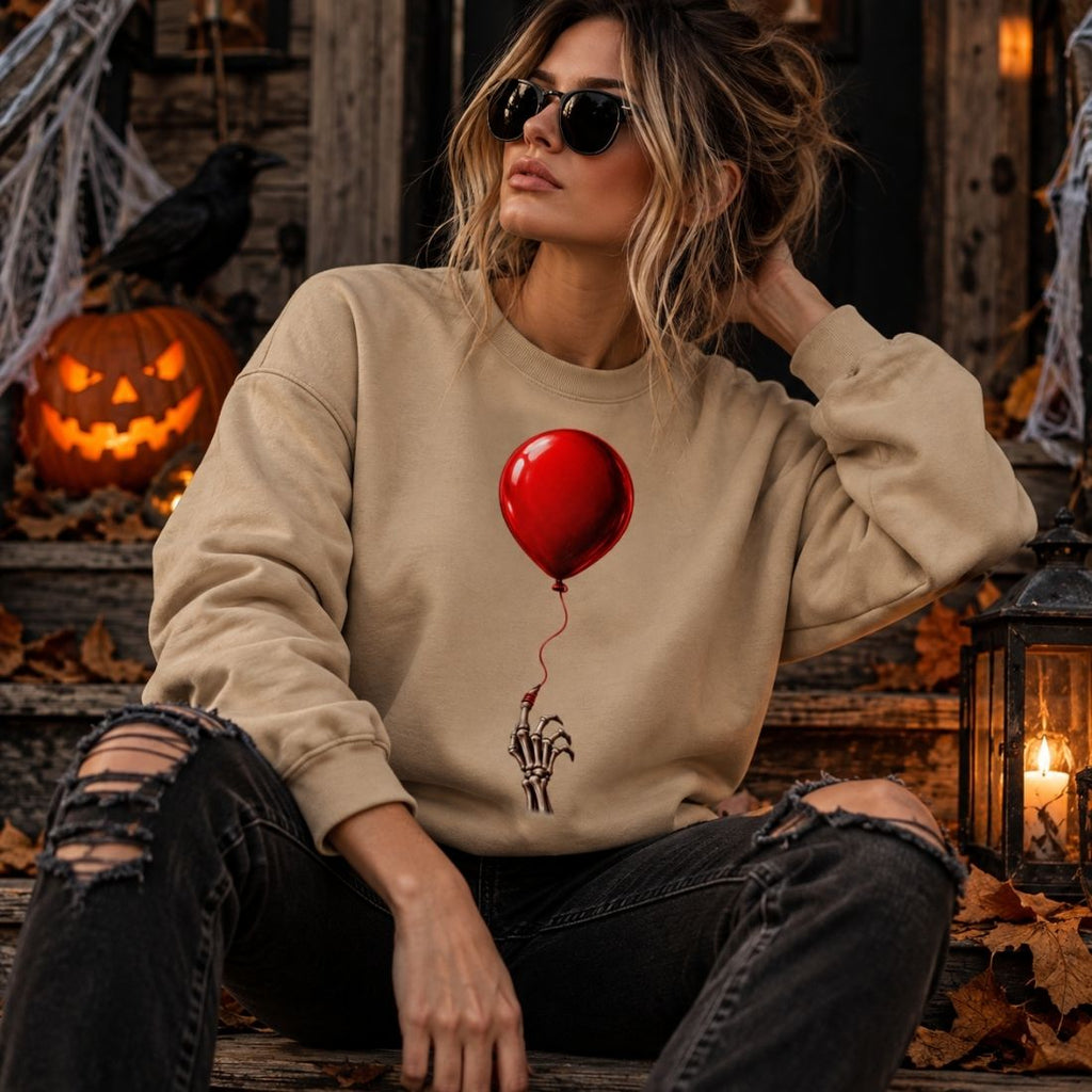 Model wearing a khaki The Last Balloon sweatshirt, ripped dark jeans and sunglasses, seated among jack-o'-lanterns and cobweb decorations.