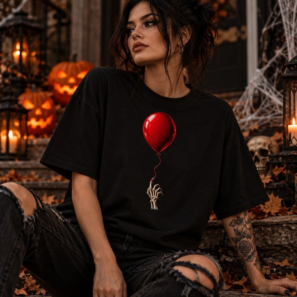 Model wearing a black The Last Balloon drop shoulder T-shirt and ripped dark jeans, seated beside pumpkins, skulls and cobweb decorations.